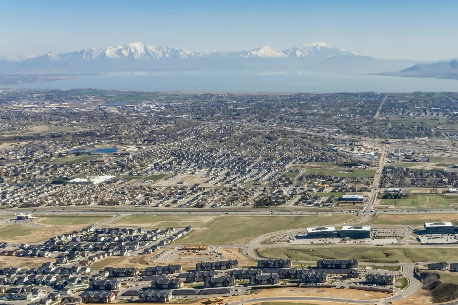 Aerial view of homes and roads with a lake and snow-covered mountains in the distance.