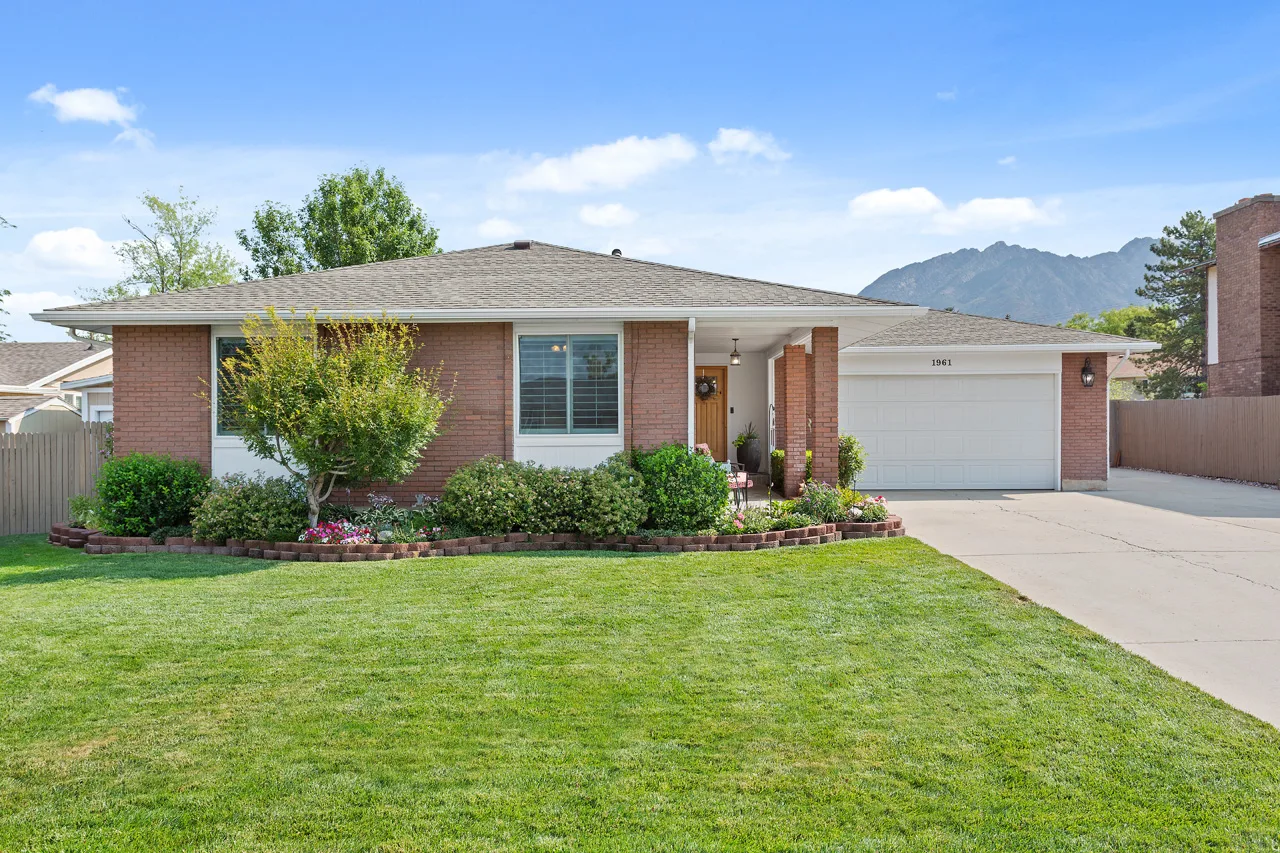 Single-story brick home with a front lawn, attached garage and mountains in the background.